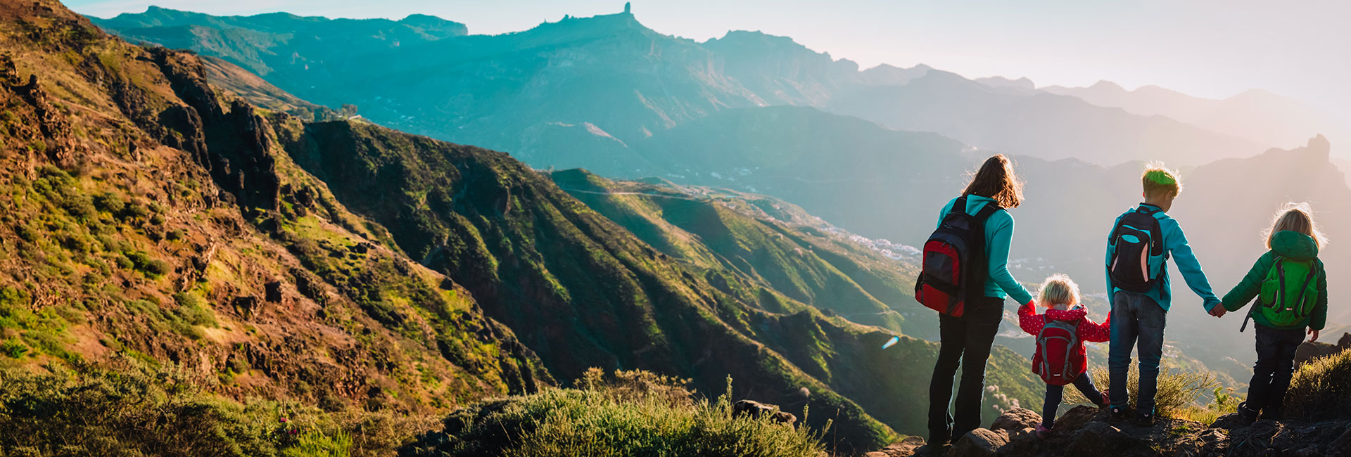 Travel nurse and children wearing backpacks and  standing on the mountain looking over. 