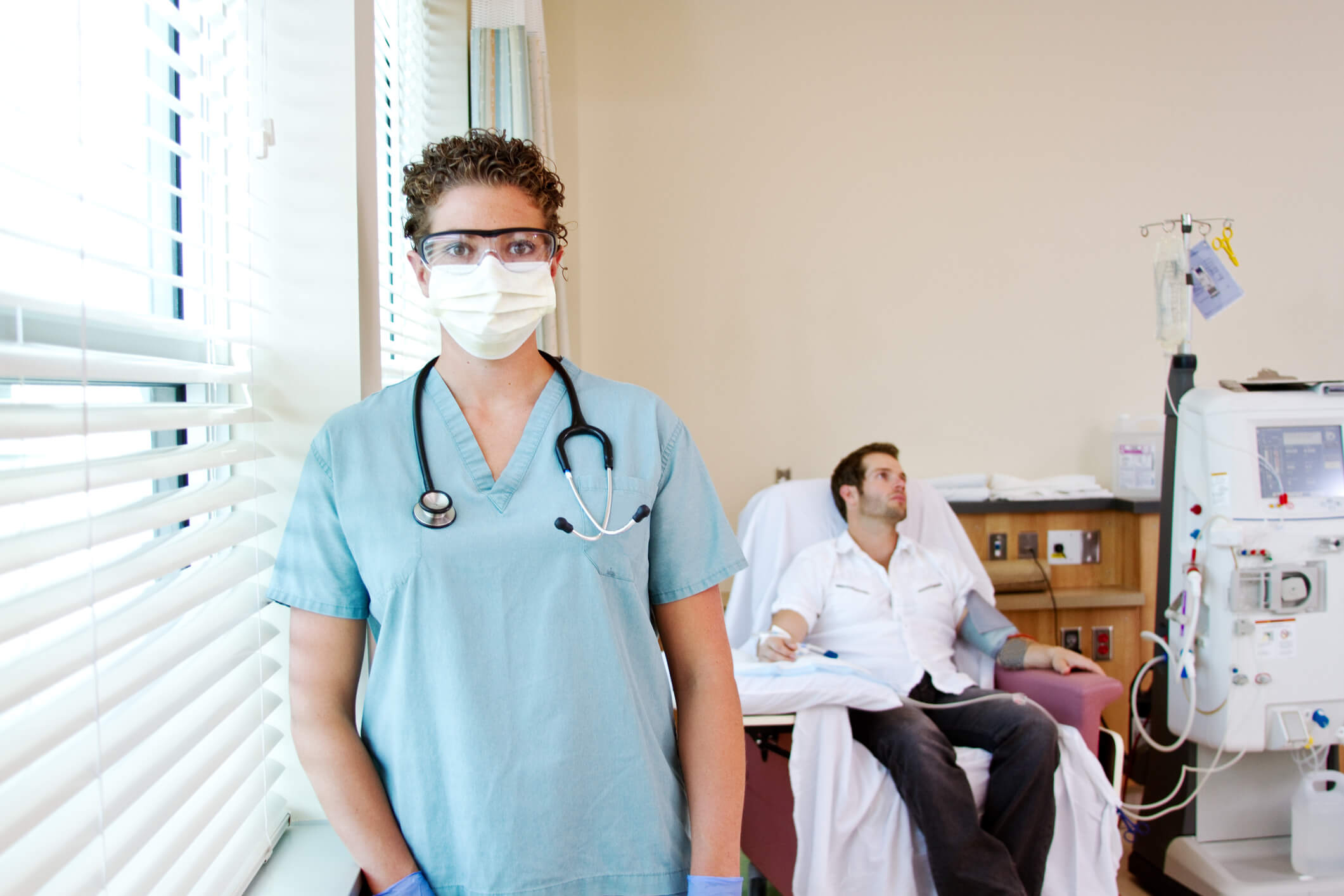 masked nurse in foreground; dialysis patient in background