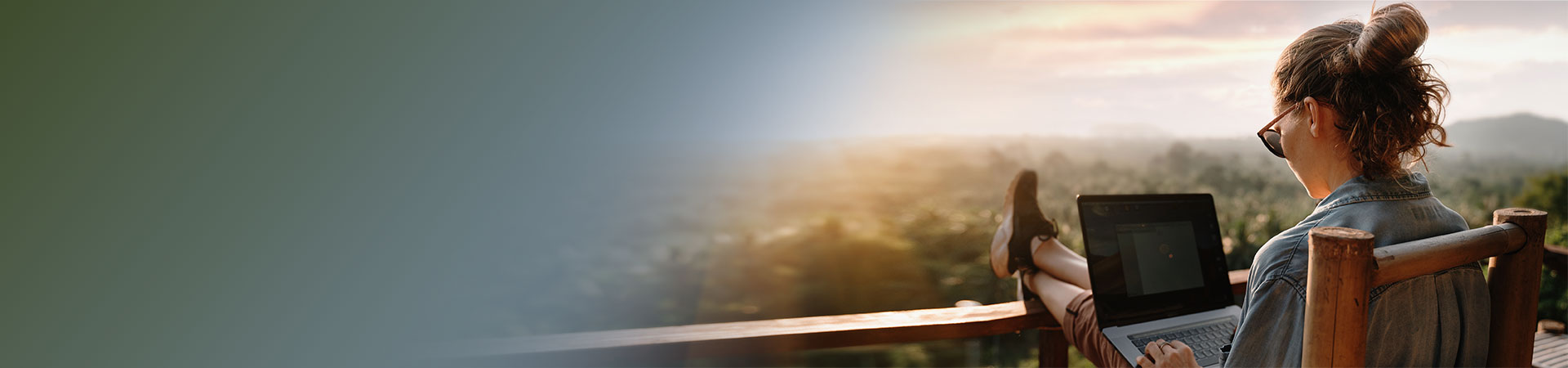 Female travel nurse sitting on porch holding a laptop with her feet propped up overlooking the mountains.